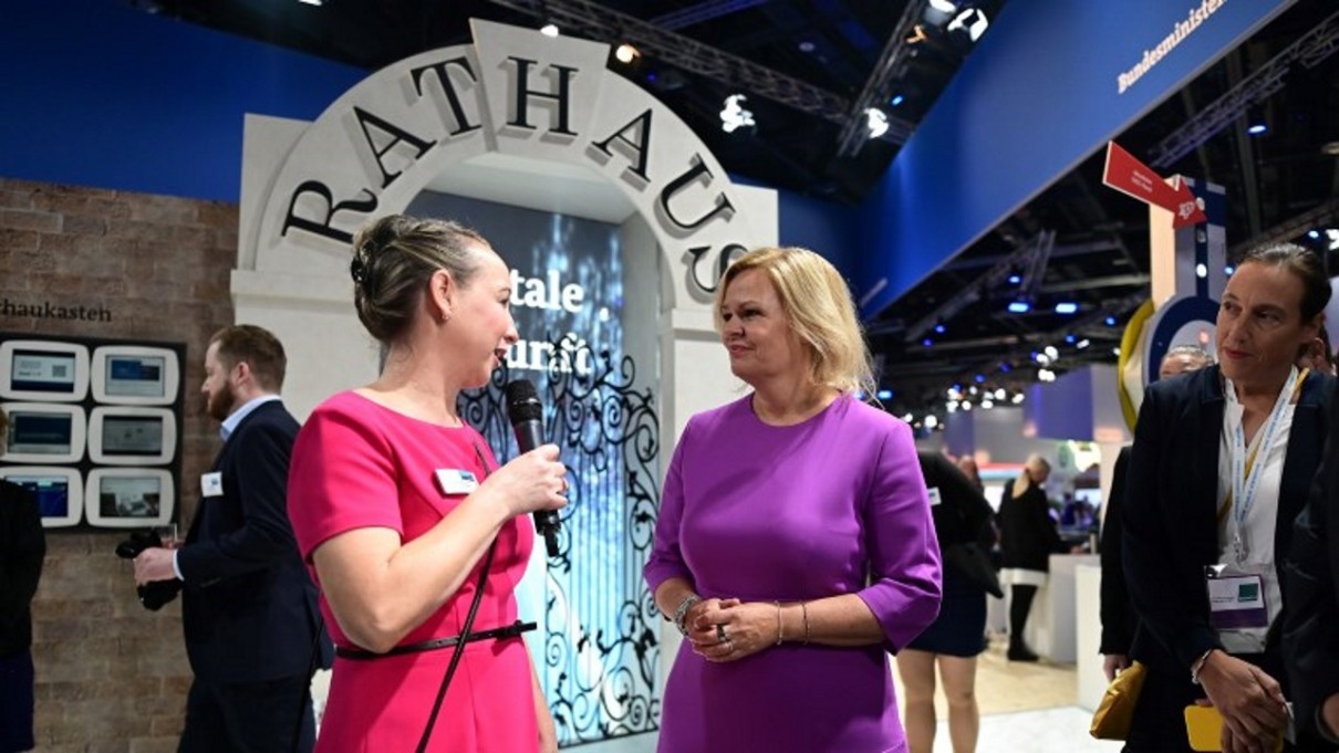 Zwei Frauen im Vordergrund, rechts Bundesinnenministerin Nancy Faeser auf dem Messestand des BMI, im Hintergrund Rathauskulisse 