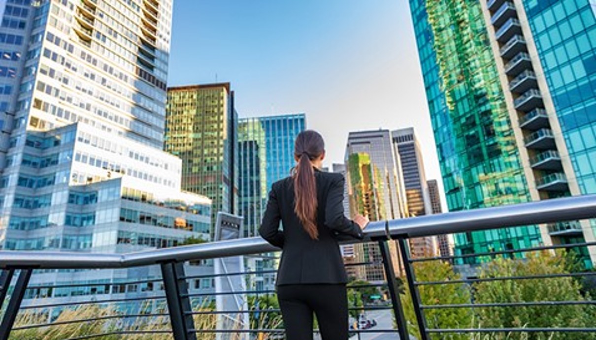 A woman from behind at a railing, in the background a city view with skyscrapers.