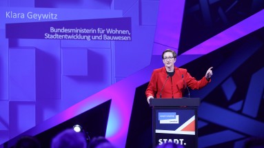 Klara Geywitz, Bundesministerin für Wohnen, Stadtentwicklung und Bauwesen setht auf der SCCON-Bühne hinter einem Rednerpult.