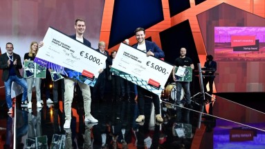 Auf der Bühne stehen zwei Männer und präsentieren die Schecks mit den 5.000 Euro Preisgeld in ihren Händen.