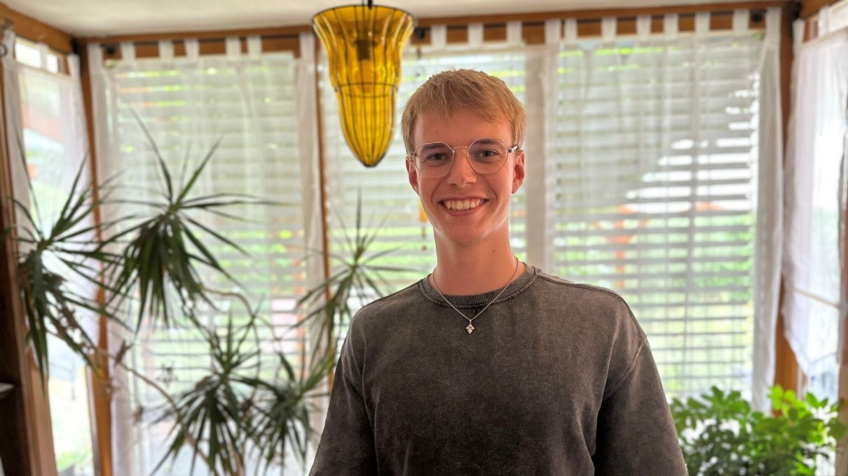 Young man in the foreground, large windows with blinds and green plants in the background. Young man in the foreground, large windows with blinds and green plants in the background.