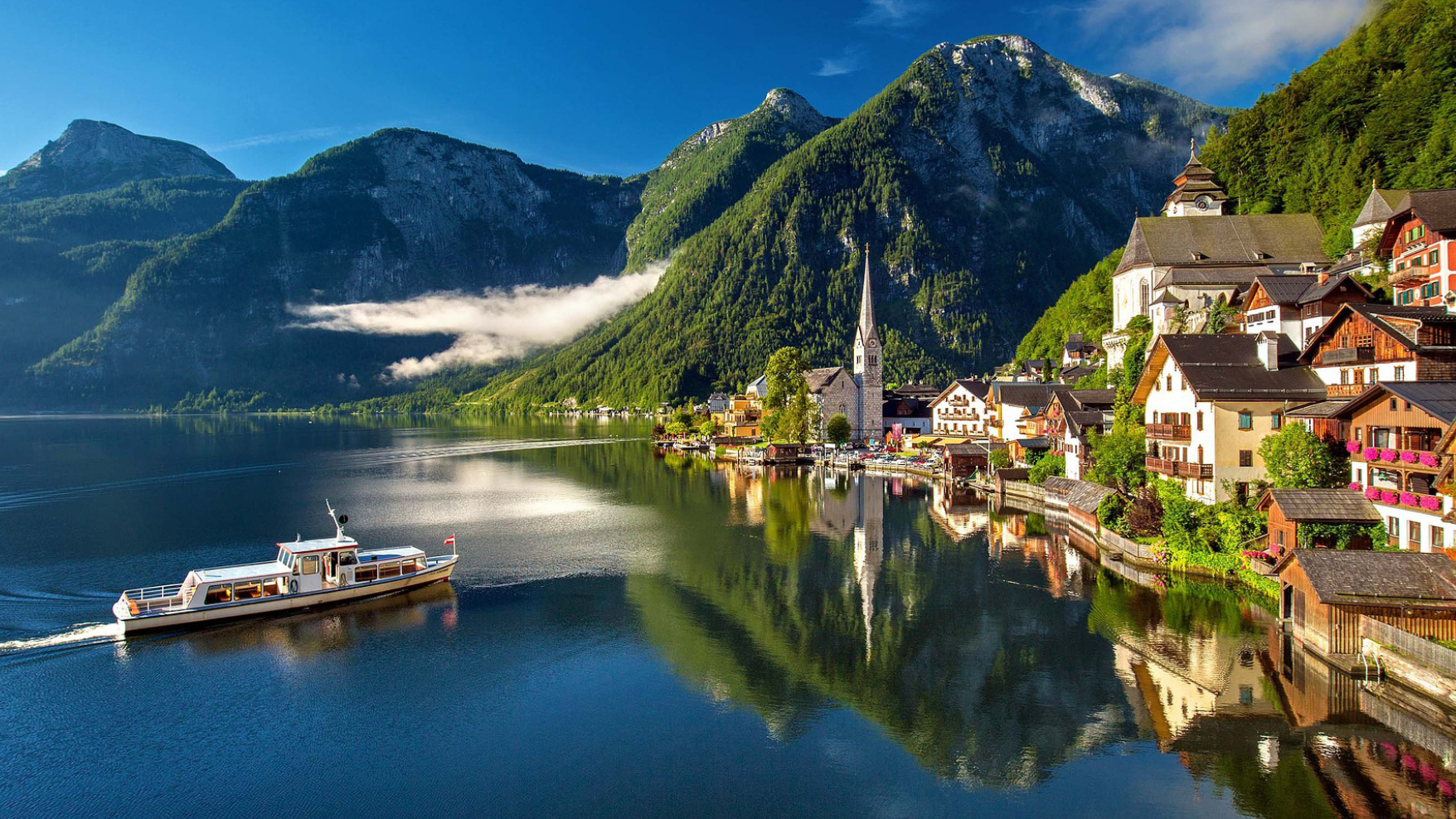 Landscape image of Austria from the mountains, with a mountain village on the right, a lake on the left and a ship on the water 