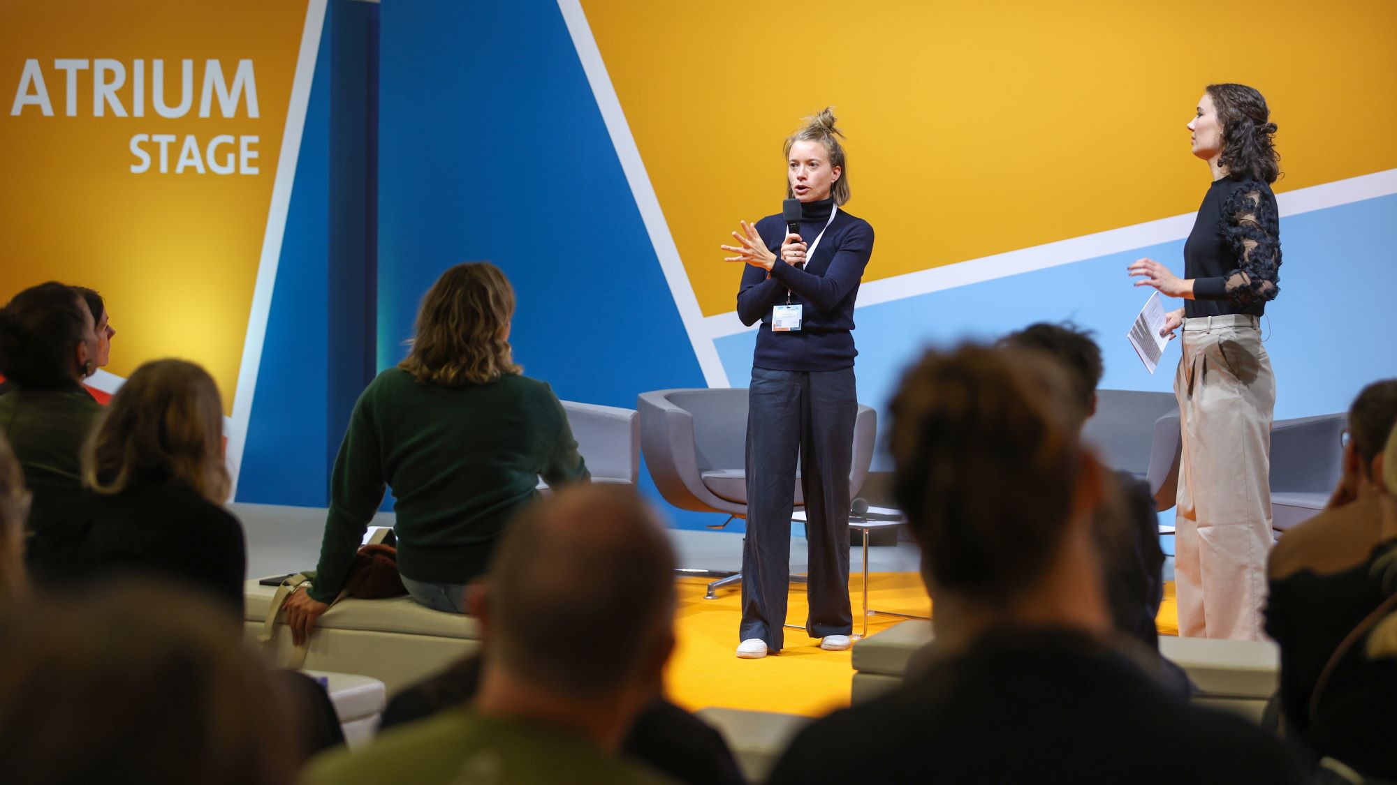 Two women give a speech on stage at SCCON. The audience sits in front and listens.