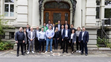 The project consortium of 19 people stands on the steps of an old building for the group photo.