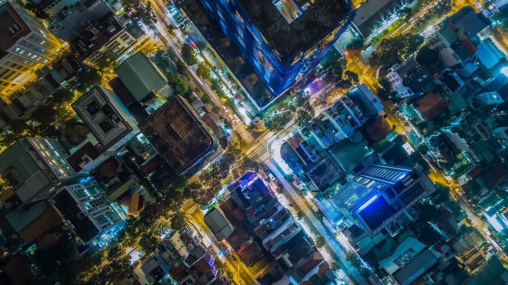 An aerial view of a city at night, showing how different neighbourhoods are connected by a network of streets and illuminated bu