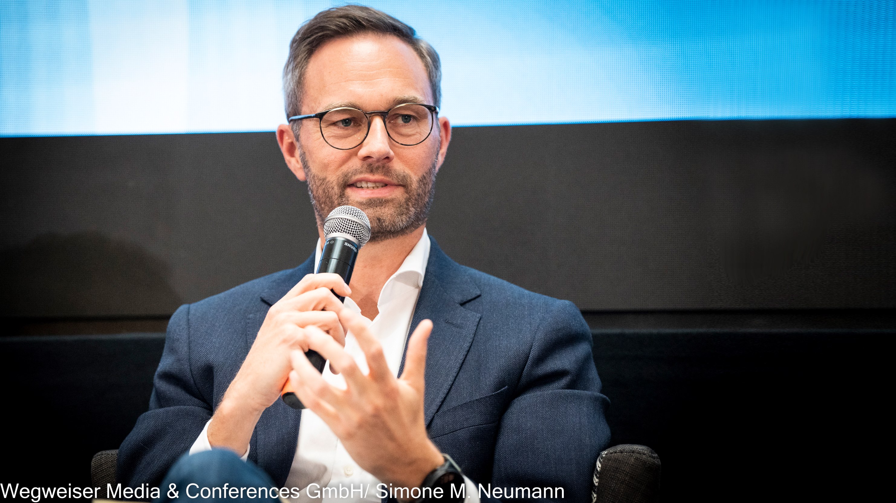 The image shows Sascha Soyk, CEO and founder of GovRadar. He is holding a microphone.