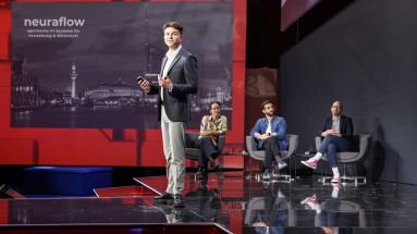 Junger Mann präsentiert auf der Bühne des Smart Country Startup Award 2024 vor einer Leinwand mit dem Schriftzug 'neuraflow'.