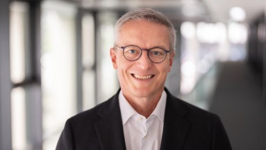 Federal Minister for Digitalzation D. Karsten Wildberger smiling, white shirt and dark jacket against a blurred background