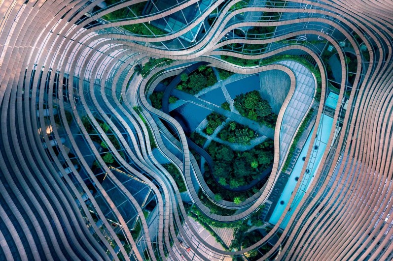 Drohnenaufnahme eines Gartens inmitten kurviger Stahlmuster. Symbolbild einer grünen Zukunftsstadt.