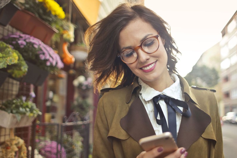 Lächelnde junge Frau nutzt Handy-App für die Teilnahme an einer städtischer Bürgerumfrage. Symbolbild für die digitale Teilhabe, Integration und Inklusion in der Smart City.